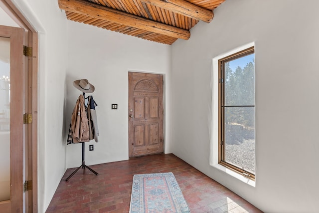 entrance foyer featuring brick floor, wooden ceiling, and beam ceiling