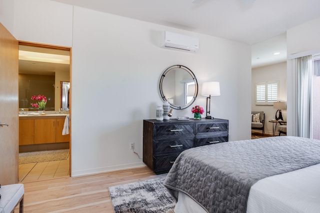 bedroom with baseboards, recessed lighting, connected bathroom, light wood-style flooring, and a wall unit AC