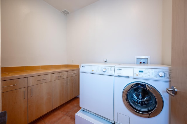 washroom with light tile patterned floors, visible vents, washing machine and clothes dryer, and cabinet space