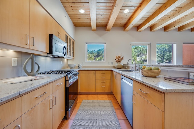 kitchen with a sink, appliances with stainless steel finishes, a peninsula, light brown cabinetry, and light stone counters