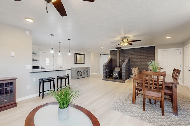 dining room with light wood-type flooring, a wood stove, a ceiling fan, and baseboards