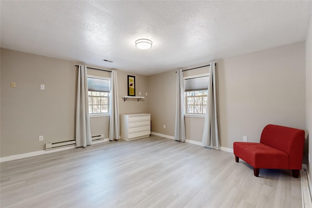 living area with a baseboard heating unit, light wood-style floors, a textured ceiling, and baseboards