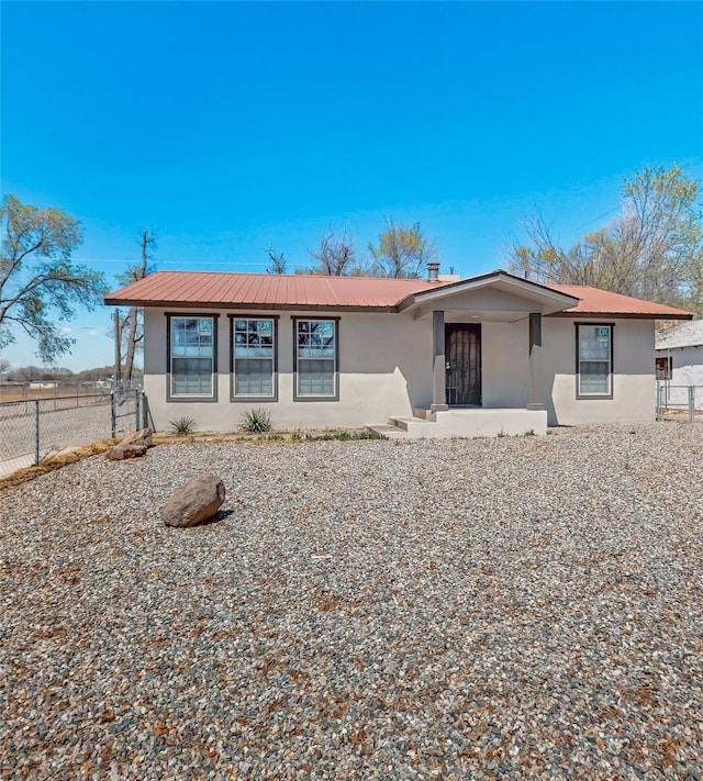 rear view of property with fence, metal roof, and stucco siding