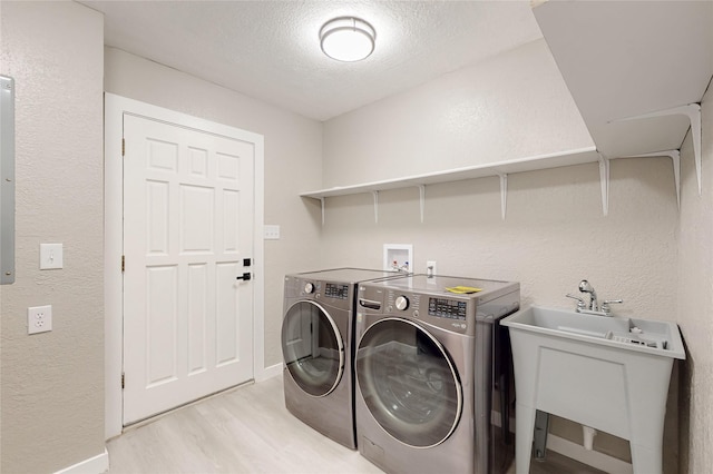 clothes washing area with washer and dryer, a textured wall, laundry area, a textured ceiling, and light wood finished floors