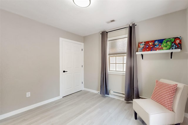 living area with wood finished floors, a baseboard heating unit, baseboards, and visible vents