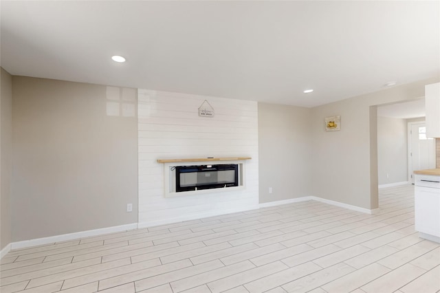 unfurnished living room with a large fireplace, baseboards, and recessed lighting