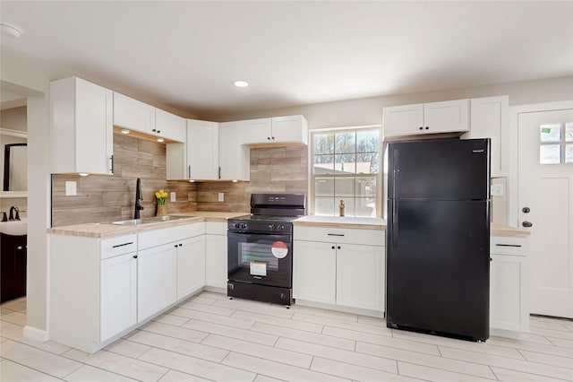 kitchen with tasteful backsplash, white cabinetry, black appliances, a sink, and light countertops