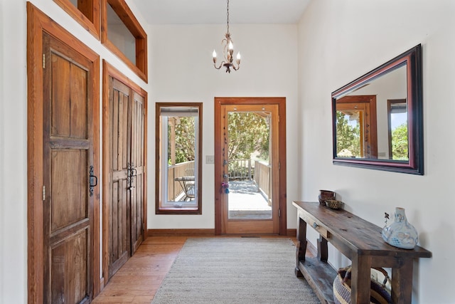 doorway with light wood-style flooring, an inviting chandelier, and baseboards