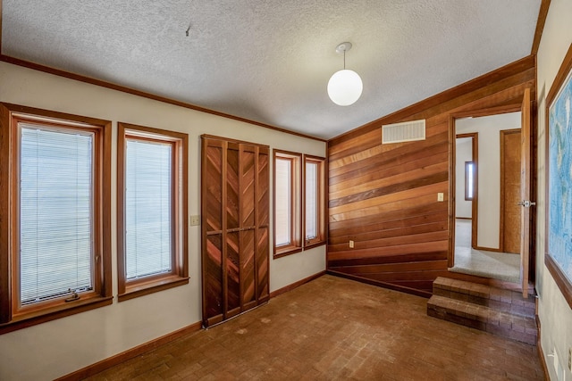 unfurnished room featuring a healthy amount of sunlight, wood walls, baseboards, and visible vents