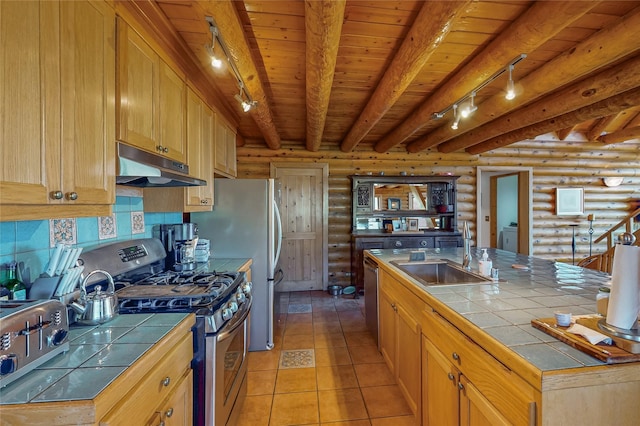 387 County Road B64, Pecos, NM 87552 - kitchen with under cabinet range hood, appliances with stainless steel finishes, log walls, tile counters, and rail lighting