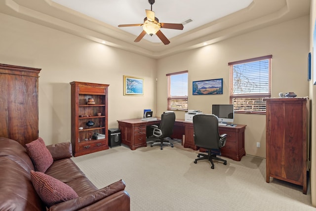 office space featuring a raised ceiling, light colored carpet, ceiling fan, and visible vents