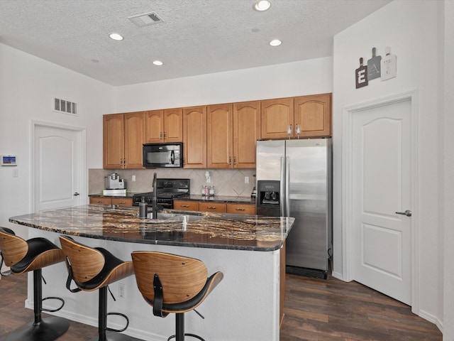 kitchen featuring stainless steel refrigerator with ice dispenser, black microwave, range with gas stovetop, a textured ceiling, and dark wood-style flooring