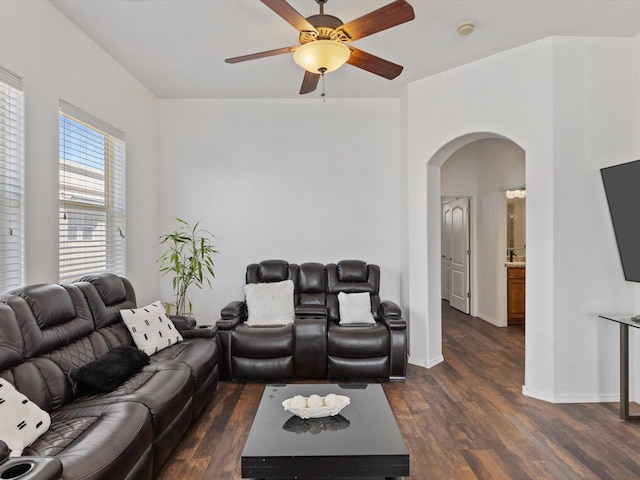 living area with arched walkways, dark wood-style flooring, a ceiling fan, and baseboards
