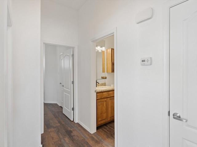 corridor with dark wood-style flooring, baseboards, and a sink