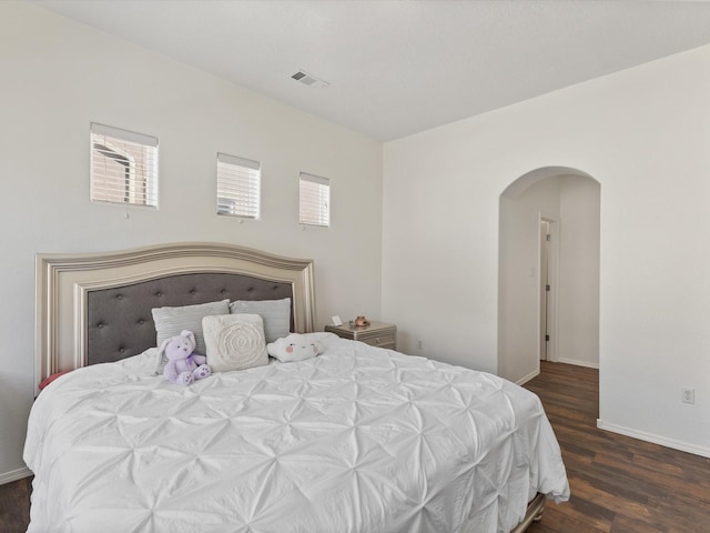 bedroom featuring arched walkways, wood finished floors, and baseboards