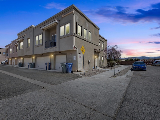 property exterior at dusk featuring a garage, driveway, and stucco siding