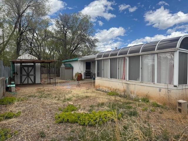 rear view of property with an outdoor structure, a sunroom, and a storage shed