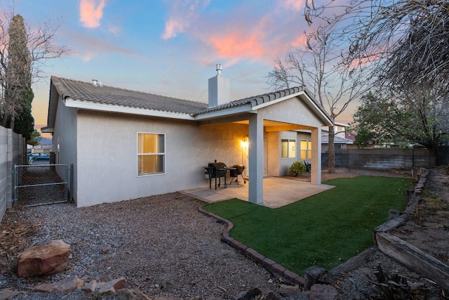 10335 Dunbar St NW, Albuquerque, NM 87114 - back of property at dusk with stucco siding, a chimney, a fenced backyard, and a lawn
