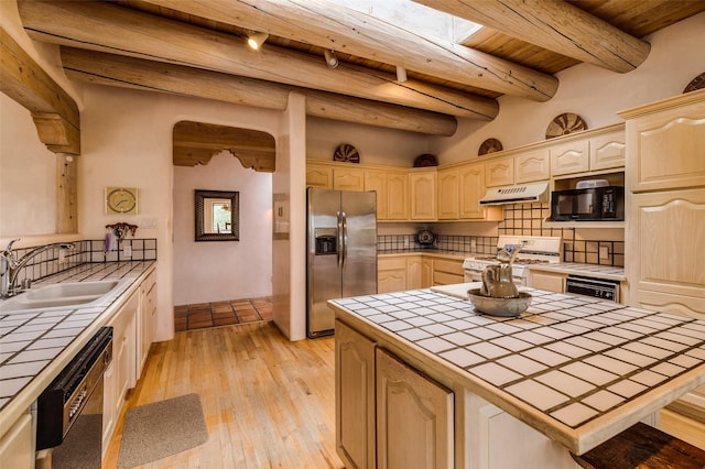kitchen featuring tile countertops, black appliances, under cabinet range hood, and a sink