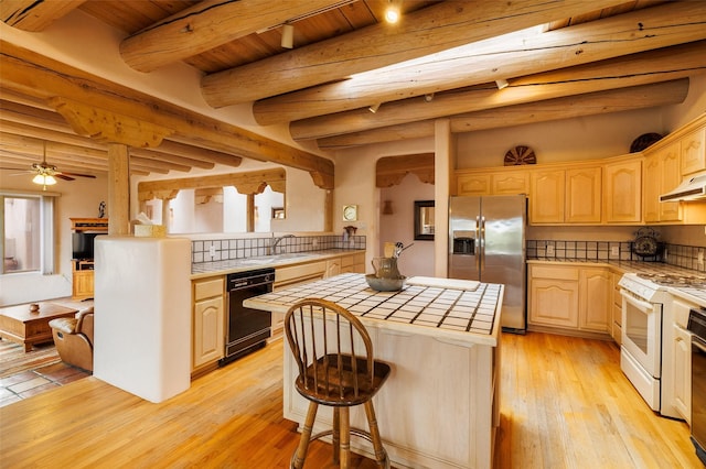 kitchen with light brown cabinetry, gas range gas stove, black dishwasher, stainless steel fridge with ice dispenser, and tile counters