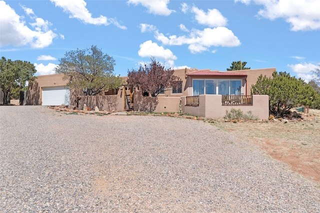 pueblo revival-style home with an attached garage, gravel driveway, and stucco siding