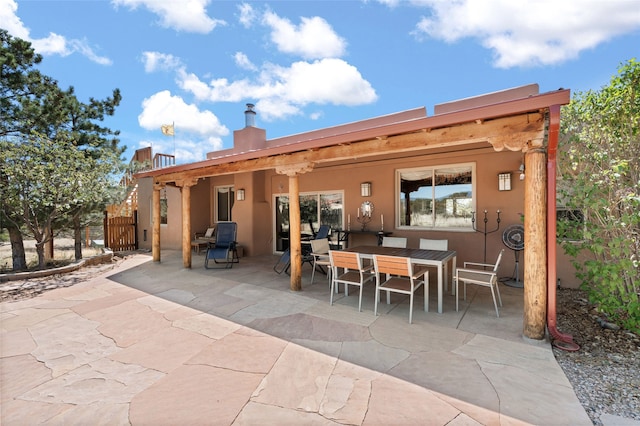 back of house featuring stucco siding, a chimney, outdoor dining area, and a patio
