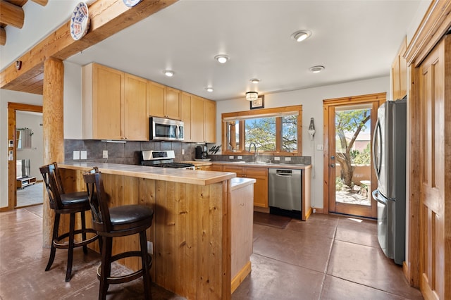kitchen featuring stainless steel appliances, backsplash, light brown cabinets, a sink, and a peninsula