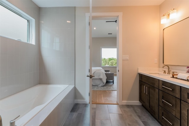 ensuite bathroom featuring tile patterned flooring, vanity, a relaxing tiled tub, baseboards, and ensuite bathroom