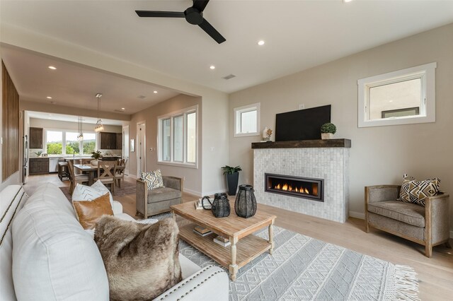 living room with ceiling fan, a tile fireplace, visible vents, and light wood-style flooring