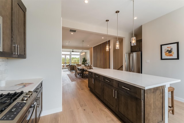 kitchen featuring light wood-type flooring, dark brown cabinets, freestanding refrigerator, light countertops, and a breakfast bar area