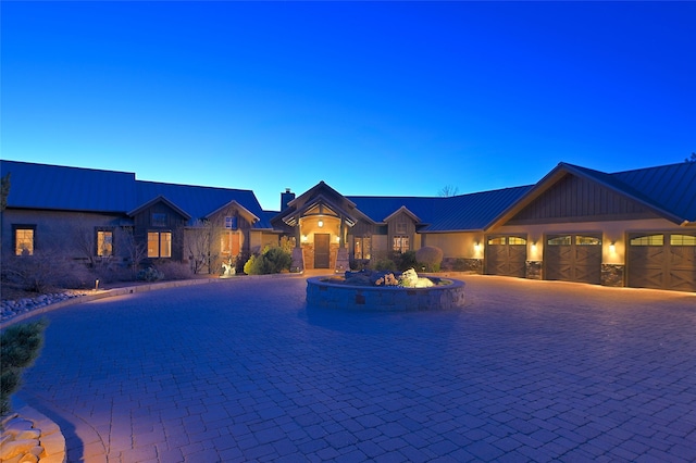 view of front of house featuring stone siding, a chimney, metal roof, a garage, and curved driveway
