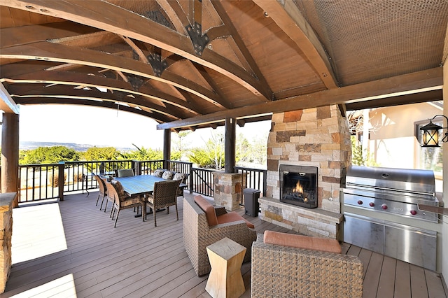 wooden terrace featuring exterior kitchen, a gazebo, an outdoor stone fireplace, outdoor dining area, and area for grilling