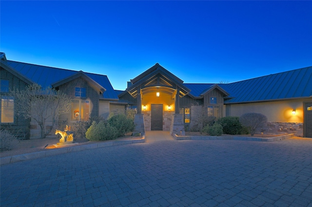 ranch-style house featuring stone siding, a standing seam roof, metal roof, and curved driveway