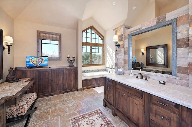 bathroom with lofted ceiling, a garden tub, stone tile flooring, and vanity