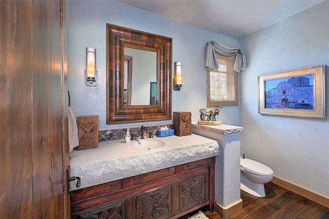 half bath with toilet, vanity, wood finished floors, and baseboards