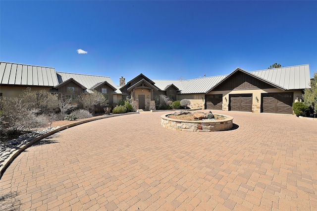 ranch-style house with stone siding, a chimney, curved driveway, and metal roof