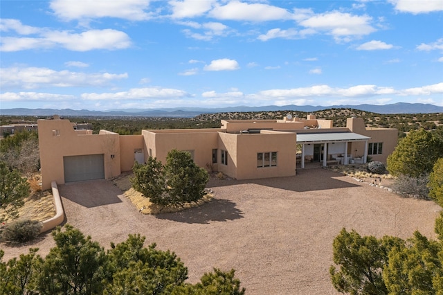 adobe home with an attached garage, driveway, a mountain view, and stucco siding