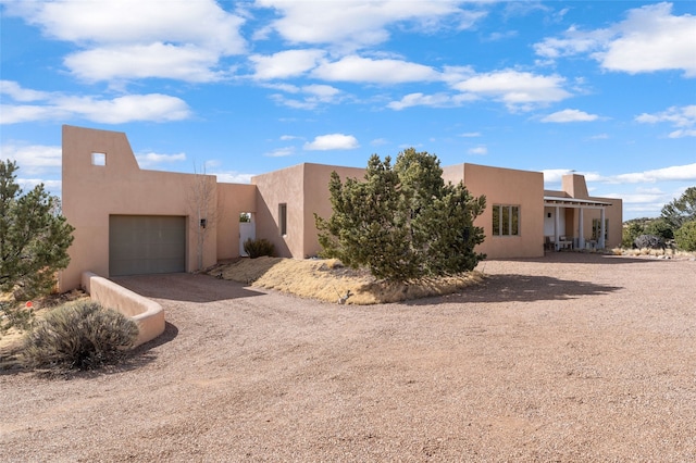 pueblo-style home featuring stucco siding, an attached garage, and dirt driveway