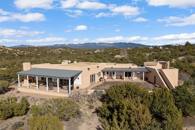 rear view of house with stucco siding, a chimney, a mountain view, and a patio