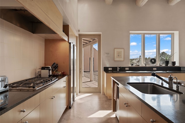 kitchen featuring wall chimney exhaust hood, a sink, stainless steel gas stovetop, decorative backsplash, and a high ceiling