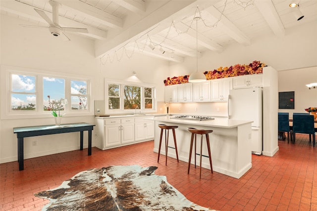 kitchen with a kitchen breakfast bar, brick floor, freestanding refrigerator, white cabinets, and a kitchen island