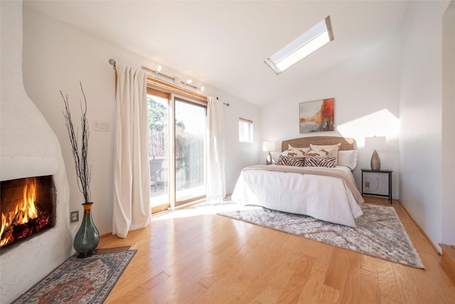 bedroom featuring a fireplace with flush hearth, wood finished floors, vaulted ceiling with skylight, and access to exterior