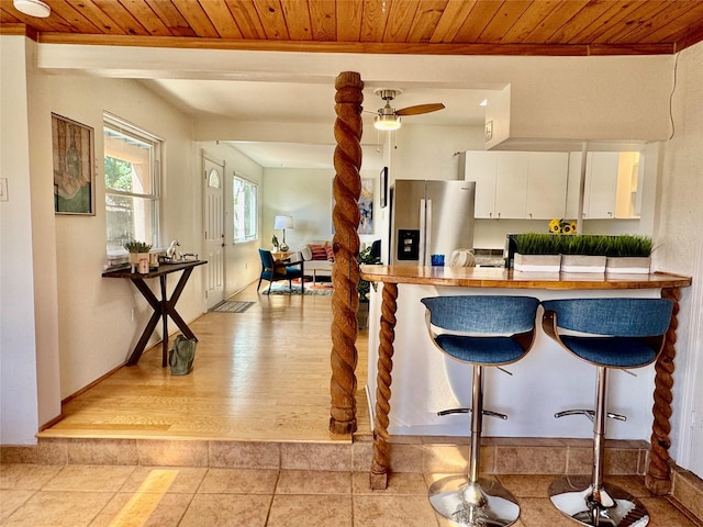 kitchen with a kitchen breakfast bar, stainless steel fridge, wood ceiling, white cabinets, and ornamental molding