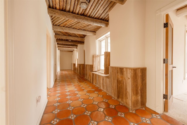 corridor featuring beamed ceiling, wooden ceiling, and wainscoting
