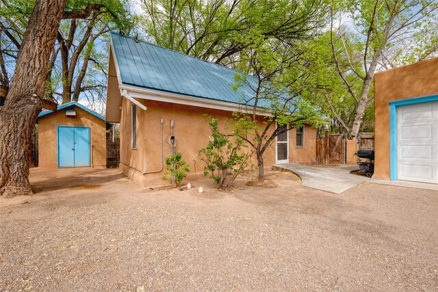 view of front of house with a storage shed, fence, an outbuilding, metal roof, and stucco siding