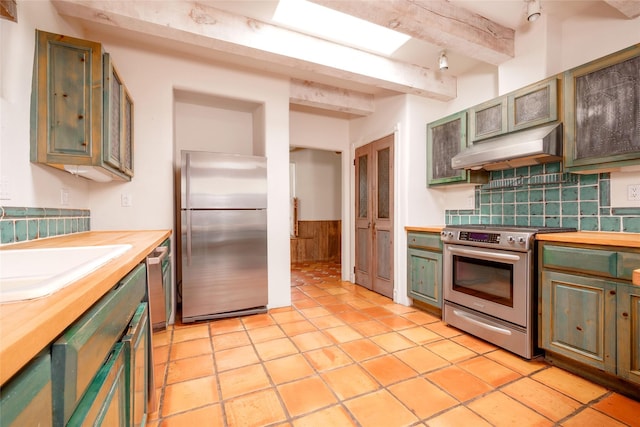 kitchen with ventilation hood, beam ceiling, wainscoting, wooden counters, and appliances with stainless steel finishes