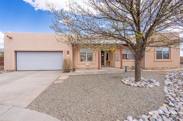 pueblo revival-style home with stucco siding, an attached garage, and concrete driveway