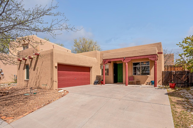pueblo-style home with fence, driveway, stucco siding, and a garage