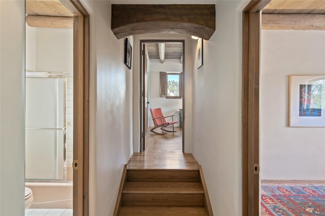 staircase featuring arched walkways, wood finished floors, and beamed ceiling