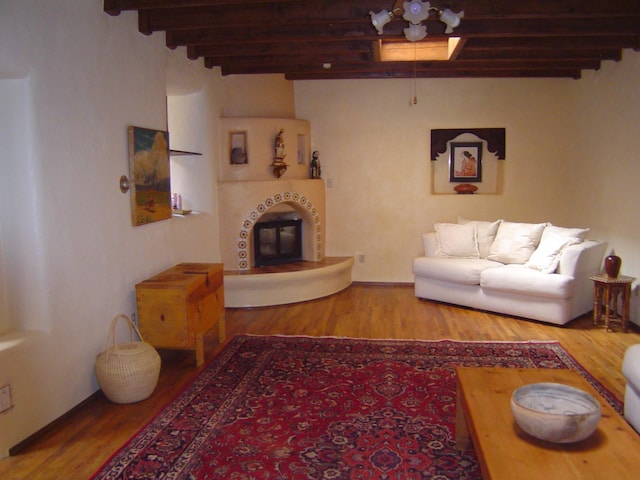 living area with wood finished floors, a tile fireplace, and beam ceiling